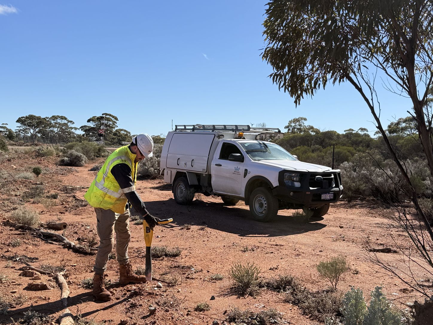 Whitech locator tracing an underground service with an electromagnetic locating receiver on a regional site, work vehicle behind