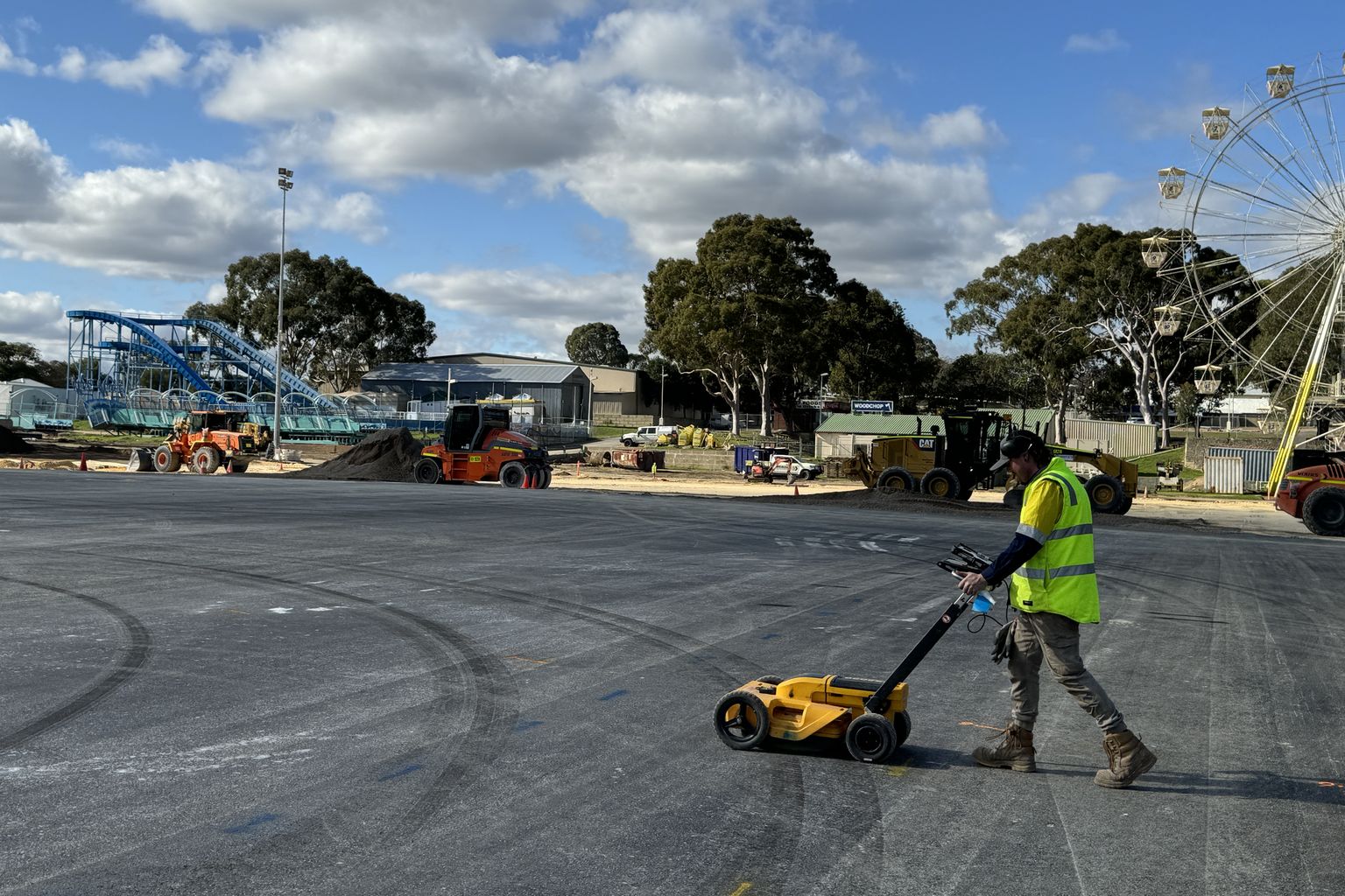 Whitech operator pushing a ground penetrating radar cart across a sealed hardstand, earthmoving plant working behind